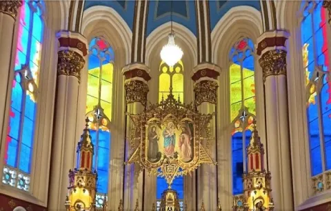 Primer plano de un vitral visto desde abajo en el que destaca la imagen de la Virgen María y de fondo los vidrios con colores amarillo, azul y rojo.