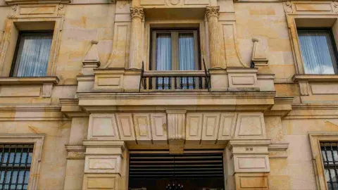 Primer plano de la fachada del edificio de frente en la que se observan tres ventanas en un segundo piso, una de ellas con un balcón.