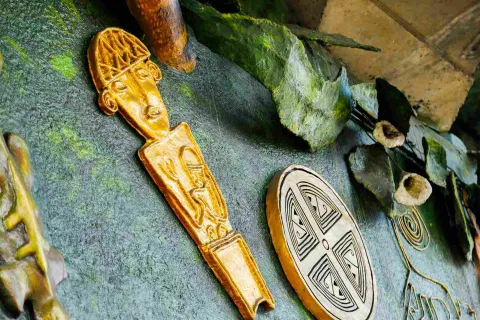 Escultura de arte indígena con figura humana dorada y diseño ovalado.