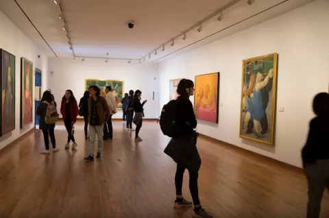 The interior of the Botero Museum's exhibition hall, where several young people are viewing paintings.