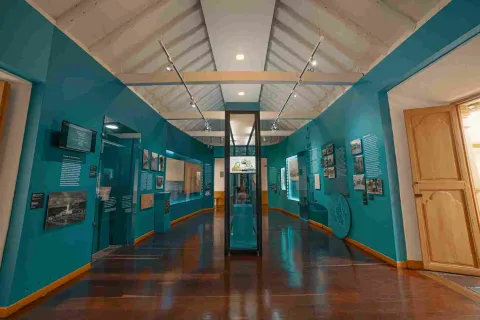 Un salón interior pintado de azul con algunos objetos en marcos de cristal sobre las paredes. En el centro hay un exhibidor de vidrio y madera.