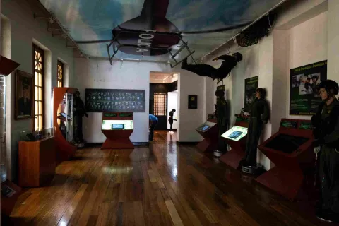 Museum interior with several mannequin-like police officer figures. A helicopter drawing with the large inscription "Police" is prominently displayed on the ceiling. A mannequin is hanging from the helicopter image.