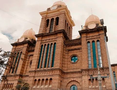 Fachada de iglesia en ladrillo vista de lado. Se observa una torre con un reloj en el centro y tres cúpulas