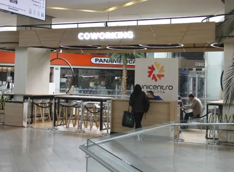 Espacio interior en el que se destaca un aviso en neón con letras blancas con una leyenda que dice: “COWORKING”. Hay un hombre joven atendiendo un stand de información en el que se lee la leyenda “Unicentro”.