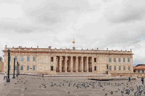 Fachada del Capitolio Nacional en piedra. Se observa al frente la Plaza de Bolívar con algunas palomas alrededor.