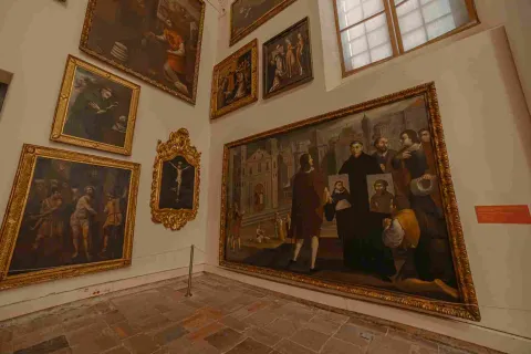 Un cuarto interior con dos paredes abarrotadas con cuadros, parece que religiosos y de época colonial.