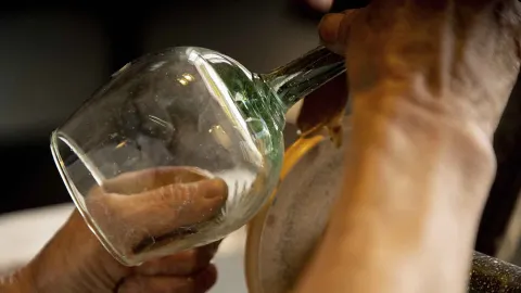 Una mano sostiene y limpia el interior de una copa de vidrio, que parece ser para vino.