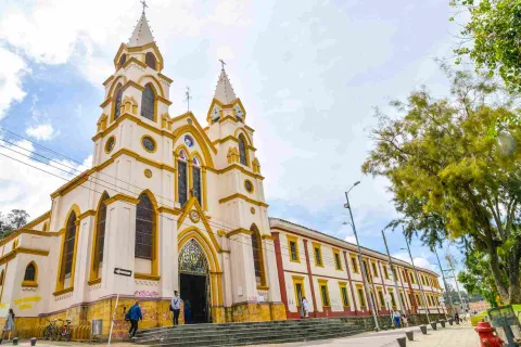 Iglesia con un campanario al lado de la calle, rodeada de árboles y un cielo despejado.