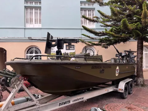 Embarcación militar de la Armada Nacional montada sobre un remolque, equipada con ametralladoras y exhibida al aire libre frente a un edificio.