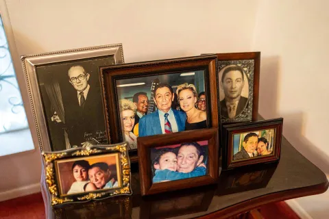Collection of framed family photographs arranged on a wooden table. The images include vintage black and white portraits and color photos from different eras, showing various people in intimate and affectionate moments.