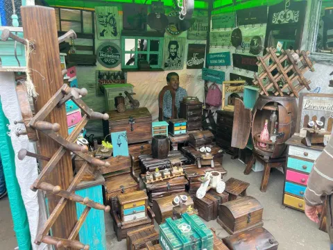 Puesto de mercado artesanal lleno de objetos decorativos de madera, como cajas, cofres, pequeños muebles y figuras talladas. Las piezas presentan acabados rústicos y algunos detalles pintados en colores vivos.
