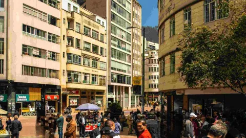  Una calle concurrida de la ciudad con personas caminando y de pie, rodeadas de edificios y tráfico.