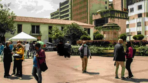  Personas de pie en un patio con edificios al fondo, disfrutando del ambiente y conversando entre sí.
