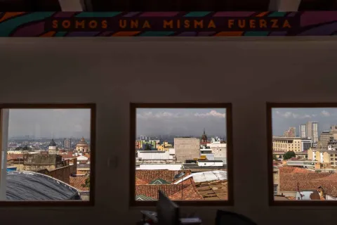  Vista de la ciudad a través de tres ventanas rectangulares desde el interior de un edificio. Se observan techos de tejas rojas, edificios del centro histórico y algunas construcciones modernas al fondo.