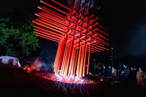  Escultura roja grande con varias personas de pie a su alrededor, admirando la obra artística en un espacio público.