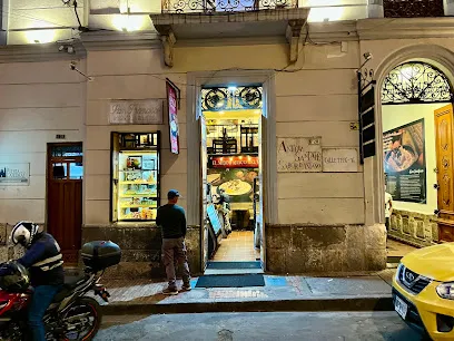 Fachada nocturna de un restaurante tradicional en una calle del centro histórico. La puerta abierta deja ver el interior iluminado con mesas dispuestas para los comensales, mientras una vitrina exhibe productos o alimentos. Afuera, una persona observa el lugar y a un costado hay motocicletas estacionadas y un taxi amarillo, típico de la ciudad.