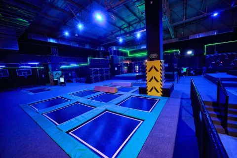 Parque de trampolines en interior con iluminación azul y detalles neón, equipado con varias zonas de salto y obstáculos.