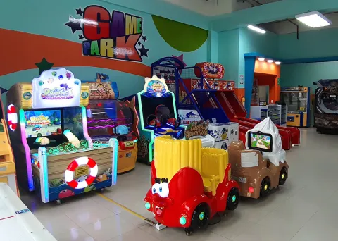  Fila de máquinas arcade en un salón de juegos, con cabinas de conducción, juegos de habilidad y luces neón en un espacio interior.