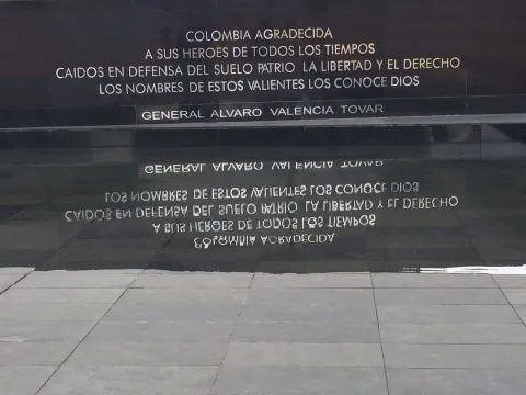 Placa conmemorativa a héroes caídos con inscripción visible en mármol negro y letras blancas con su reflejo en agua. Hay una leyenda que dice: “COLOMBIA AGRADECIDA A SUS HÉROES DE TODOS LOS TIEMPOS CAÍDOS EN DEFENSA DEL SUELO PATRIO, LA LIBERTAD Y EL DERECHO LOS NOMBRES DE ESTOS VALIENTES LOS CONOCE DIOS. GENERAL ÁLVARO VALENCIA TOVAR”