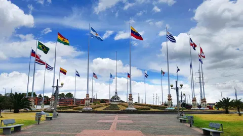 Plaza del Monumento a las Banderas con múltiples banderas ondeando y senderos abiertos bajo cielo nublado.
