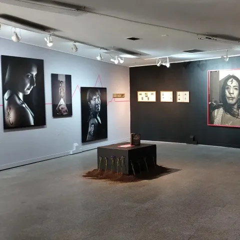  Sala de museo con exposición de retratos fotográficos y una instalación central en el piso.