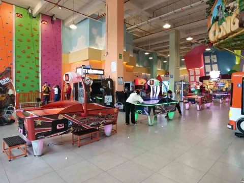 Área de juegos arcade en interior con mesas de air hockey, máquinas recreativas y un muro de escalada al fondo.