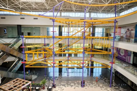 Estructura de circuito de cuerdas y obstáculos suspendidos en varios niveles dentro de un centro comercial amplio y luminoso.