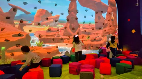 Niños en una piscina de pelotas interactuando con una proyección de ciudad animada en una gran pantalla, con elementos de videojuego visibles.