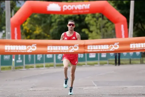 A runner crosses the finish line alone during a race, with an arch and finish line tape in the background.