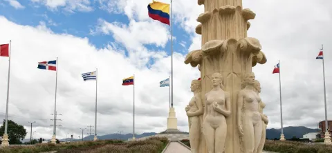 Detalle del Monumento a las Banderas con esculturas de mujeres y banderas ondeando, incluida la de Colombia, bajo cielo nublado.