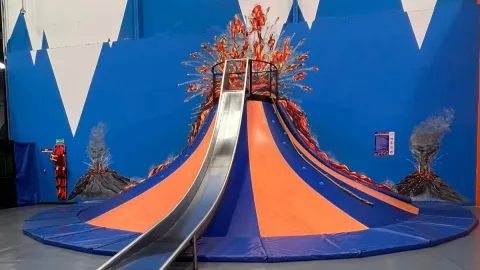  Estructura de juego con forma de volcán en un parque interior, con tobogán central y decoración de erupción en las paredes.