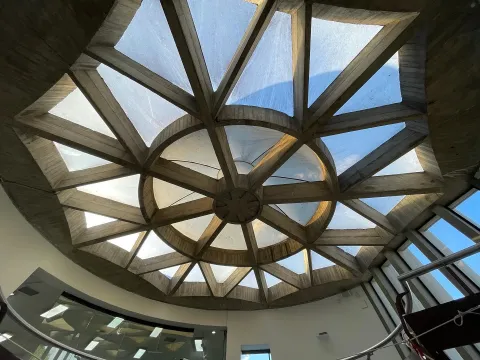 Cúpula de vidrio y concreto con diseño geométrico que deja entrar luz natural en un espacio interior.