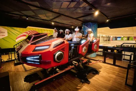 Grupo de personas usa gafas de realidad virtual en un simulador de movimiento con forma de vehículo futurista dentro de un espacio recreativo interior.