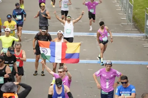 Runners celebrate crossing the finish line, some raising their arms and one holding a tricolor flag.