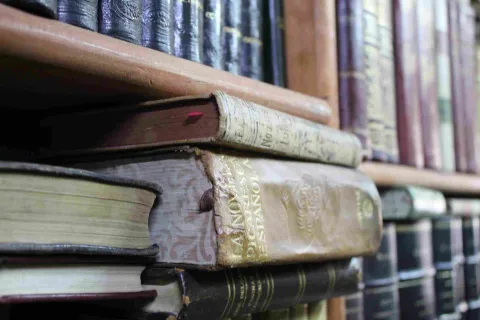 Antique books stacked and on shelves, with worn covers and embossed details.