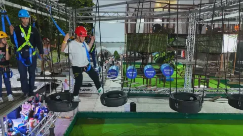 Personas con arnés y casco cruzan un circuito de llantas suspendidas en un parque de aventuras.
