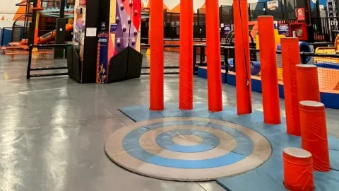 Zona de obstáculos con postes acolchados rojos y plataformas en un parque de aventura interior, diseñada para juegos de equilibrio y agilidad.