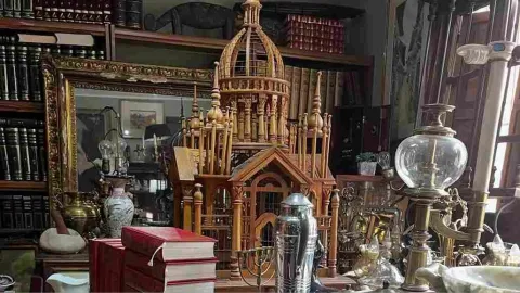 Table with antique and decorative objects, books, and a wooden model in a vintage bookstore.