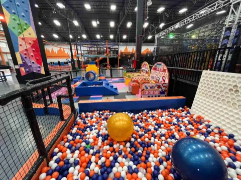 Zona de juegos infantiles en un parque interior con piscina de pelotas, estructuras coloridas y áreas de actividades para niños.