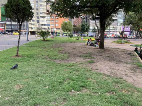 Zona verde urbana con árboles y personas descansando en un parque de Bogotá, rodeado de edificios y vías de la ciudad.