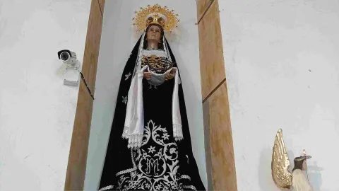 Escultura de la Virgen de los Dolores vestida de negro y blanco, con corona dorada y expresión solemne, ubicada en un nicho dentro de una iglesia.