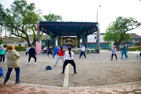 Grupo de personas realizando actividad física al aire libre frente a un escenario en la plaza de Bosa.