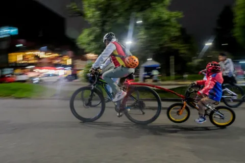 An adult and a child cycle through the streets of Bogotá during the Ciclovía at night, an experience that combines sport, family, and urban life under the city lights.