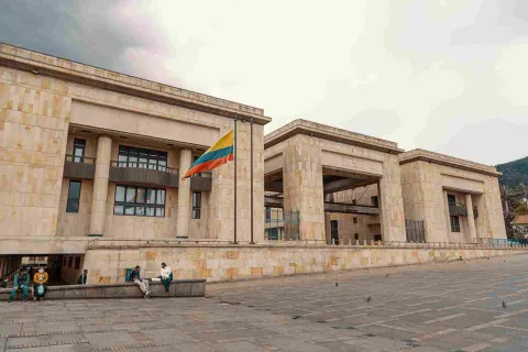 Fachada de estructura con tres edificaciones en piedra. Sobresale al frente izada una bandera de Colombia.