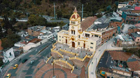 Plano general de una iglesia vista desde arriba. La iglesia es de color marrón claro y está rodeada por edificaciones y calles por las que circulan automóviles.