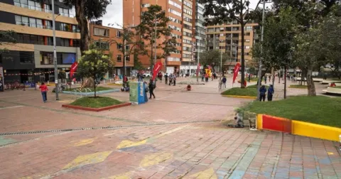 Plazoleta peatonal en Chapinero con zonas verdes, árboles y personas transitando entre edificios residenciales y comerciales de Bogotá.