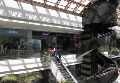 Interior of the Gran Estación shopping mall with escalators, shops, and a modern structure illuminated by natural light.