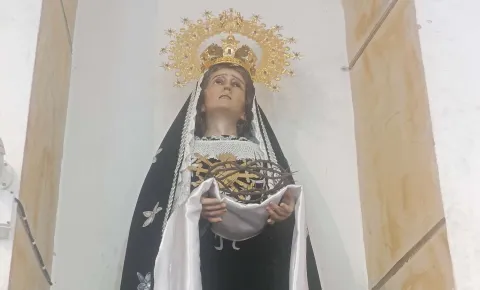 Primer plano de la Virgen de los Dolores con corona dorada, sosteniendo una corona de espinas, ubicada en un nicho de iglesia.
