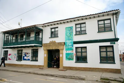  Edificio blanco de la Alcaldía Local de Bosa, con balcones verdes y personas en la entrada.
