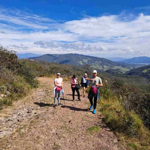 Personas realizan una caminata ecológica por un sendero de montaña con paisajes naturales y cielo despejado.